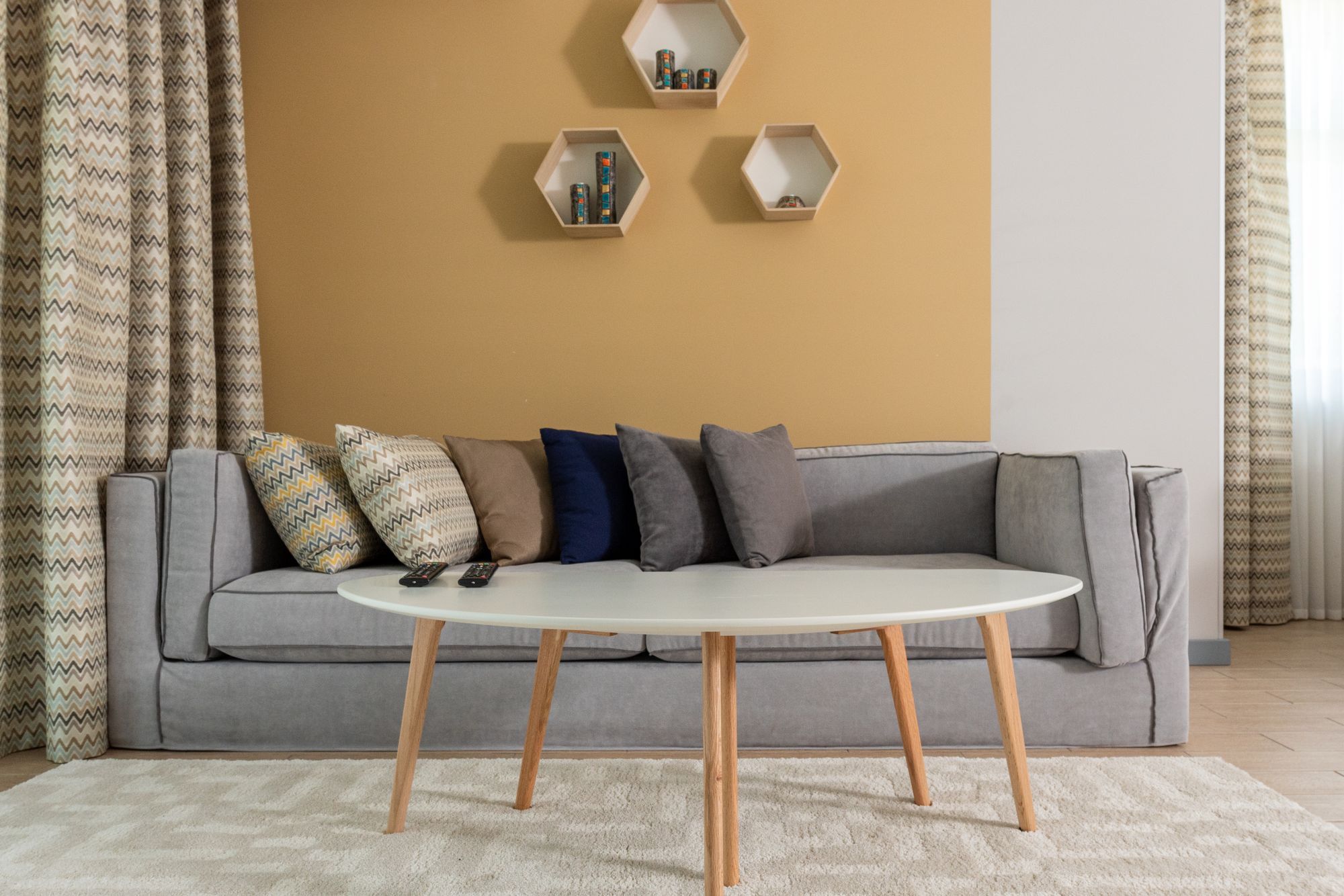 Graues Sofa vor einer ockergelb gestrichenen Wand mit drei sechseckigen Regalen